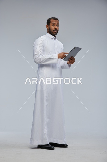 رجل سعودي بالثوب الأبيض يستخدم جهازاً لوحياً