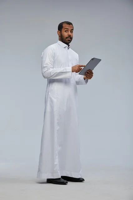 رجل سعودي بالثوب الأبيض يستخدم جهازاً لوحياً