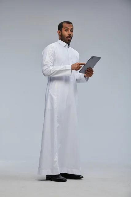رجل سعودي بالثوب الأبيض يستخدم جهاز لوحي بتعبير مندهش