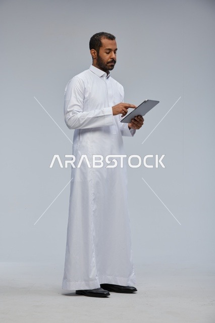 رجل سعودي بالثوب الأبيض يستخدم جهاز لوحي