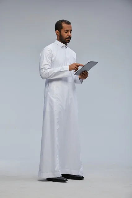 رجل سعودي بالثوب الأبيض يستخدم جهاز لوحي