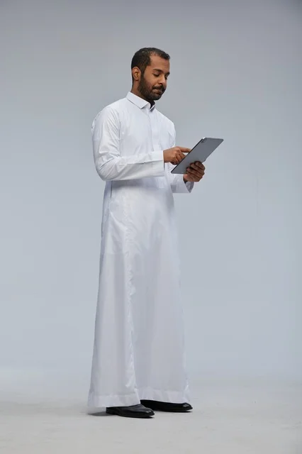 Saudi Man in White Thobe Using Digital Tablet