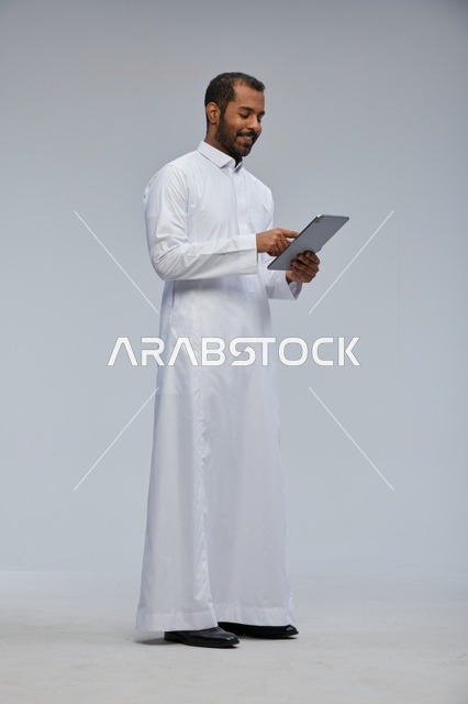 رجل سعودي بالثوب الأبيض يستخدم جهاز لوحي