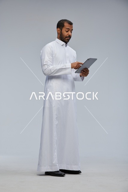 رجل سعودي بالثوب الأبيض يستخدم جهاز لوحي