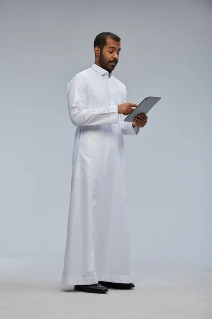 Saudi Man in White Thobe Using Digital Tablet
