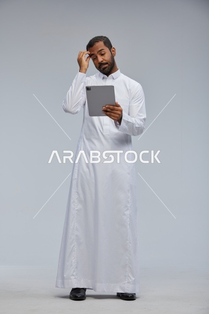 رجل سعودي بالثوب الأبيض يستخدم جهاز لوحي بتعبير محتار