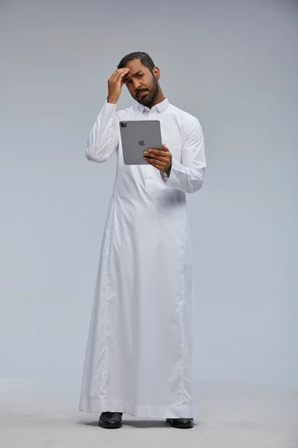 رجل سعودي بالثوب الأبيض يستخدم تابلت بتعبير حائر