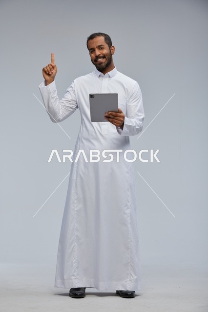 رجل سعودي بالثوب الأبيض يستخدم جهازاً لوحياً