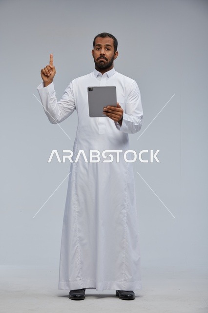 رجل سعودي بالثوب الأبيض يستخدم جهاز لوحي