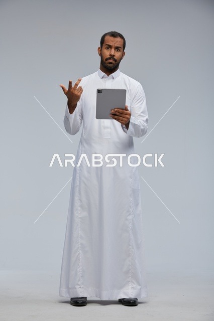 رجل سعودي بالثوب الأبيض يستخدم جهازاً لوحياً خلفية رمادية