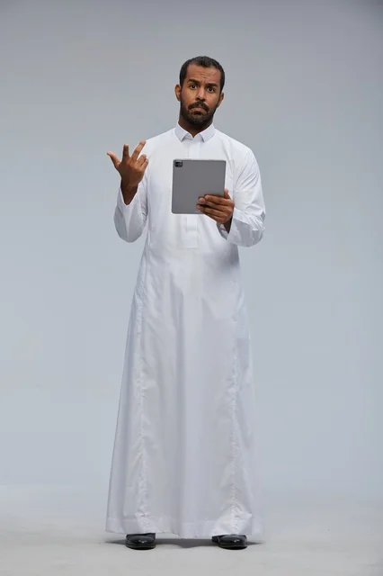 رجل سعودي بالثوب الأبيض يستخدم جهازاً لوحياً خلفية رمادية