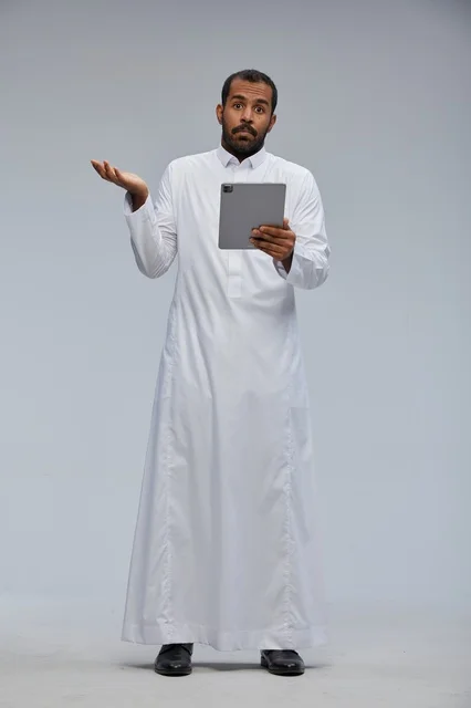 رجل سعودي بالثوب يحمل جهاز لوحي مندهش في الاستوديو
