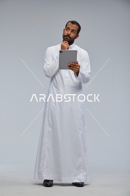 رجل سعودي بالثوب الأبيض يفكر باستخدام جهاز لوحي