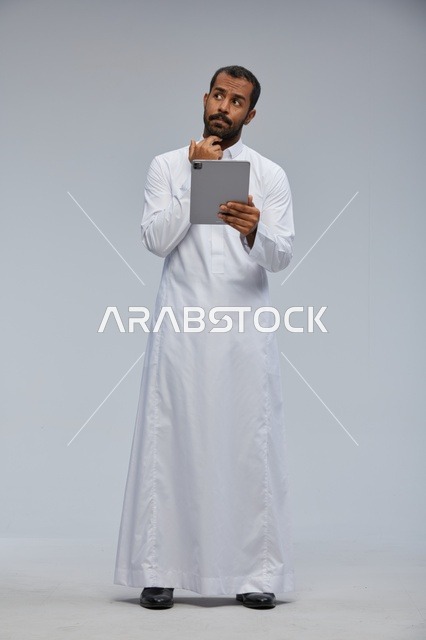 رجل سعودي بثوب أبيض يستخدم جهازًا لوحيًا
