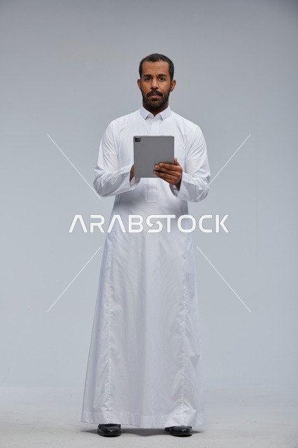 رجل سعودي بالثوب الأبيض يستخدم جهاز لوحي