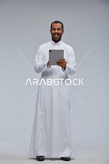 رجل سعودي بالثوب الأبيض يمسك جهازاً لوحياً