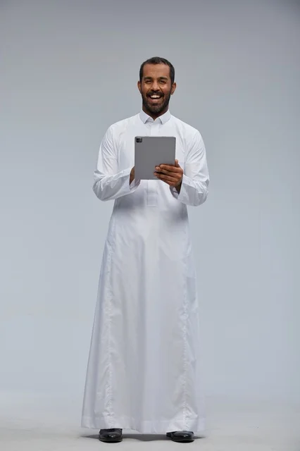 رجل سعودي بالثوب الأبيض يمسك جهازاً لوحياً