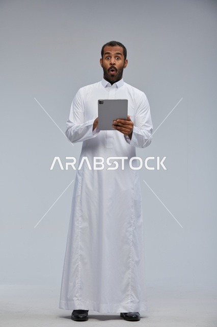 رجل سعودي بالثوب الأبيض يستخدم جهاز لوحي بملامح مصدومة