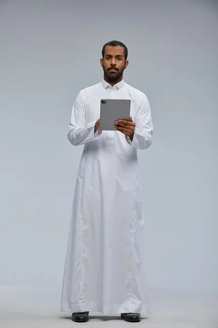 رجل سعودي بالثوب الأبيض يستخدم جهازاً لوحياً في الاستوديو