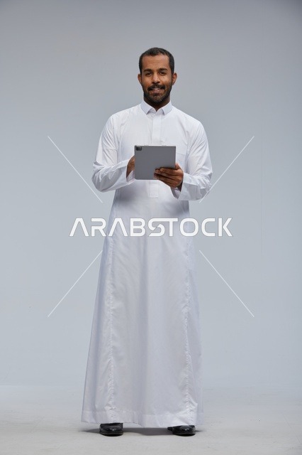 رجل سعودي بالثوب الأبيض يستخدم جهازاً لوحياً