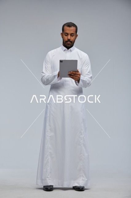 رجل سعودي بثوب أبيض يستخدم جهازًا لوحيًا