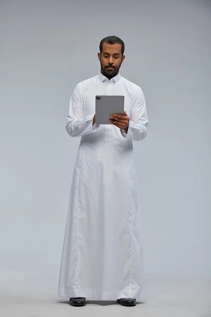 رجل سعودي يرتدي الثوب الأبيض يستخدم جهازاً لوحياً في الاستوديو