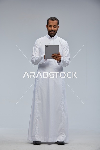 رجل سعودي بالثوب الأبيض يستخدم جهاز لوحي في الاستوديو