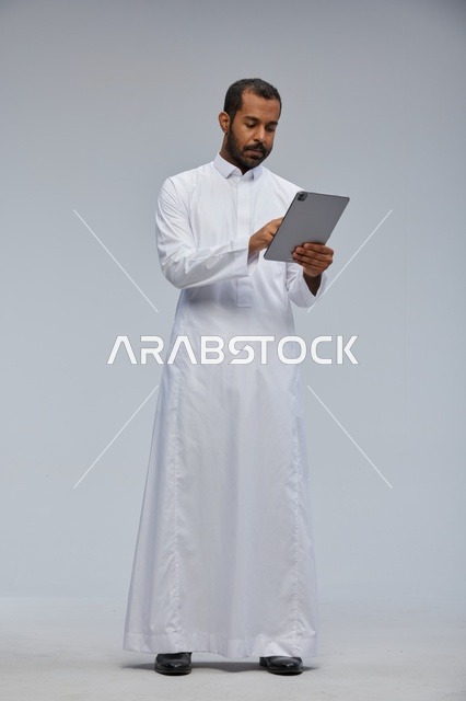 رجل سعودي بالثوب الأبيض يستخدم جهازاً لوحياً