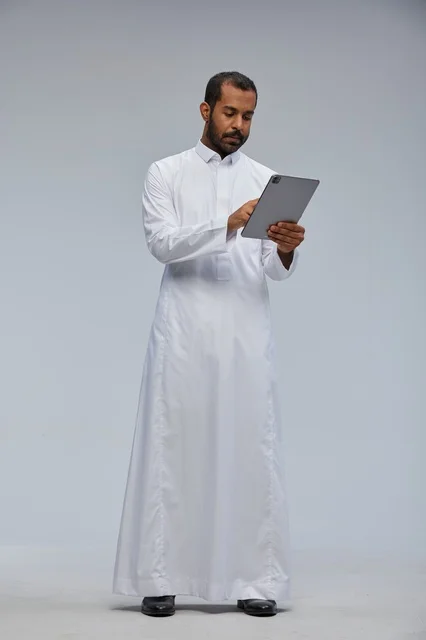 رجل سعودي بالثوب الأبيض يستخدم جهازاً لوحياً