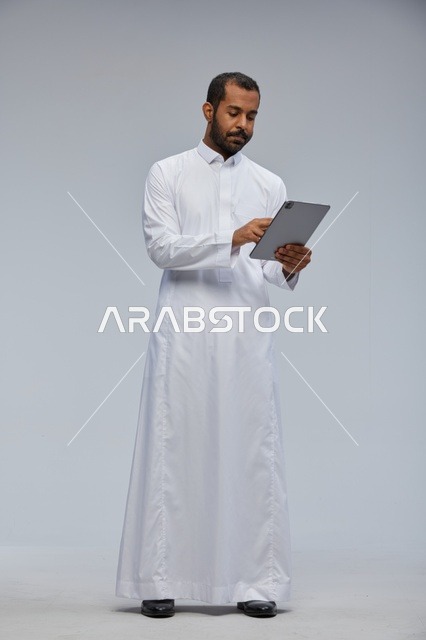 رجل سعودي بالثوب الأبيض يستخدم جهازاً لوحياً في الاستوديو