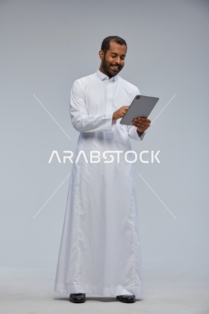 رجل سعودي بالثوب الأبيض يستخدم جهازاً لوحياً في الاستوديو