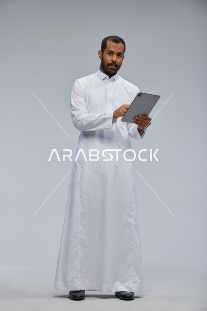 رجل سعودي بالثوب الأبيض يستخدم جهاز لوحي بالاستوديو