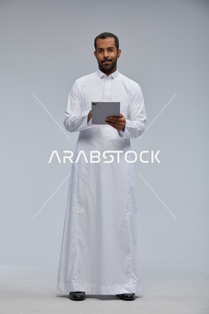 Saudi Man in Thobe Using Tablet on Grey Background