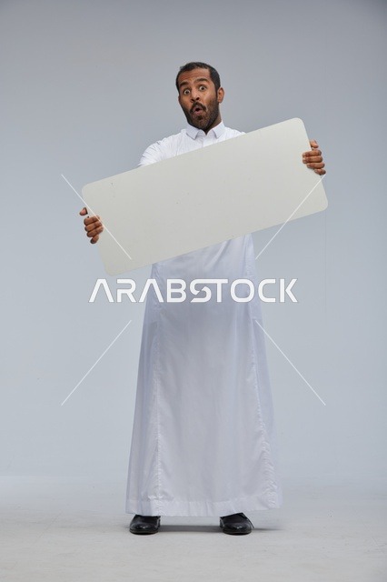 رجل سعودي مندهش يحمل لوحة بيضاء فارغة بالثوب