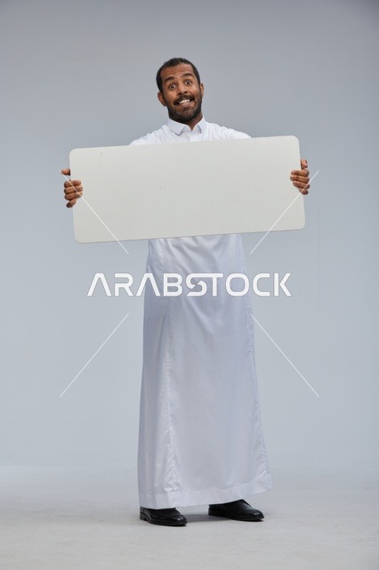 رجل سعودي مبتسم يحمل لوحة فارغة بالزي التقليدي