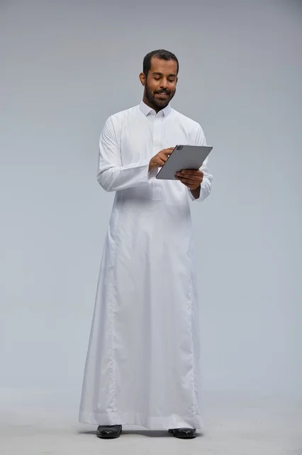 رجل سعودي بالثوب الأبيض يستخدم جهازاً لوحياً
