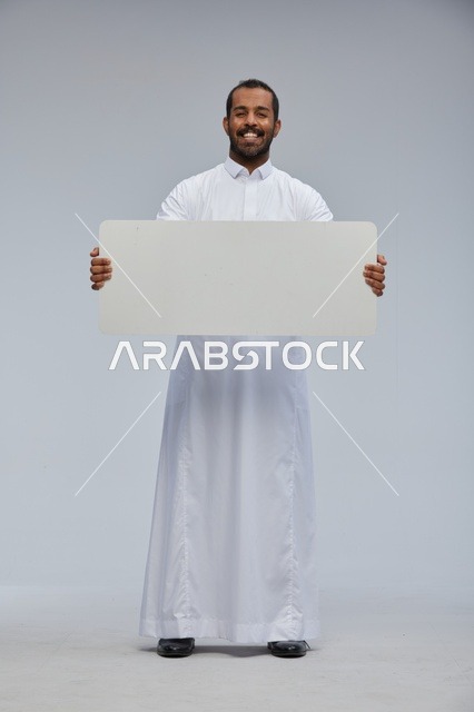 رجل سعودي مبتسم يحمل لوحة بيضاء فارغة في الاستوديو