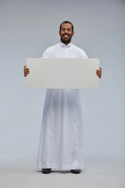 رجل سعودي مبتسم يحمل لوحة بيضاء فارغة في الاستوديو