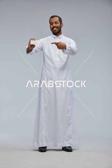 رجل سعودي يرتدي الثوب التقليدي يمسك بطاقة بيضاء فارغة