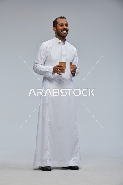 رجل سعودي مبتسم بالثوب التقليدي يحمل كوب قهوة