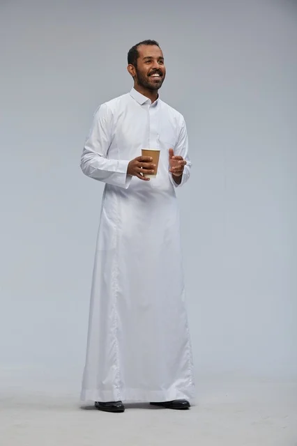 رجل سعودي مبتسم بالثوب التقليدي يحمل كوب قهوة