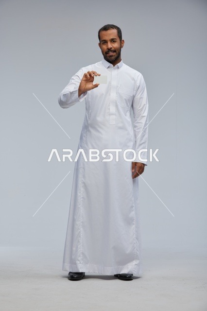 رجل سعودي يرتدي الثوب التقليدي يحمل بطاقة بيضاء فارغة