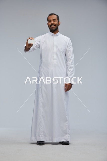 رجل سعودي مبتسم يمسك بطاقة عمل فارغة في الاستوديو