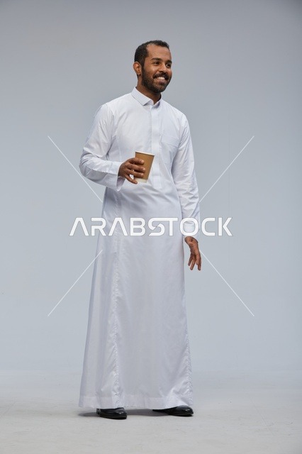 رجل سعودي بالثوب الأبيض التقليدي يحمل كوب قهوة