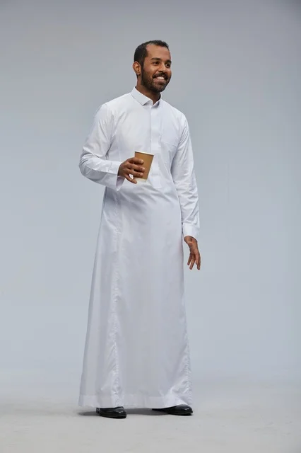رجل سعودي بالثوب الأبيض التقليدي يحمل كوب قهوة