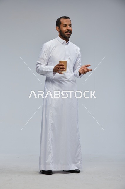 رجل سعودي بالزي التقليدي يحمل كوب قهوة مبتسماً