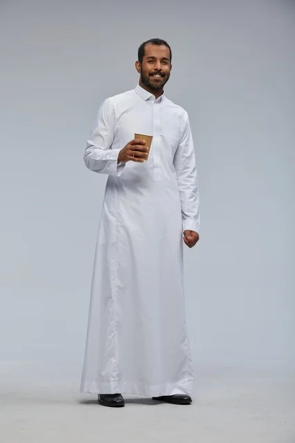 رجل سعودي مبتسم بالزي التقليدي يحمل كوب قهوة