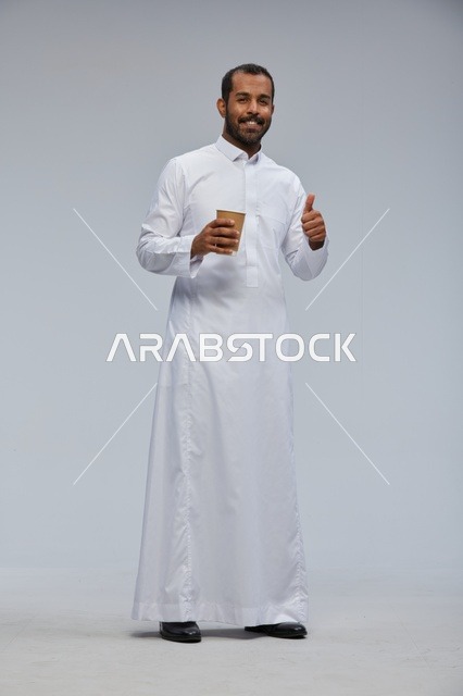 رجل سعودي مبتسم يحمل كوب قهوة بالزي التقليدي