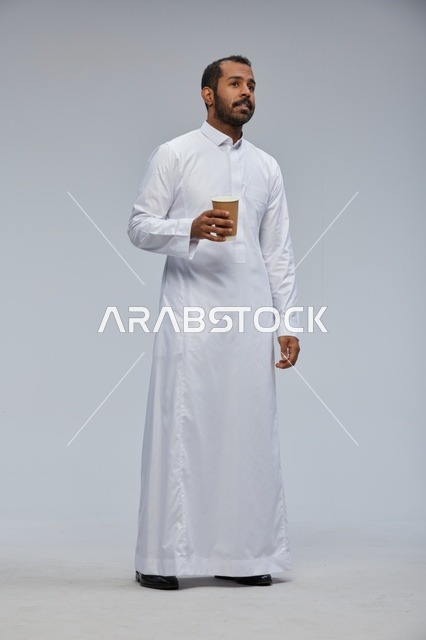 رجل سعودي مبتسم يحمل كوب قهوة بالثوب الأبيض