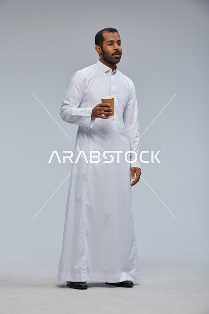 رجل سعودي بالثوب الأبيض يحمل كوب قهوة في الاستوديو